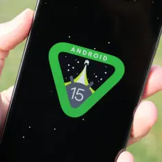 Dłoń trzyma smartfon z logo Android 15 na czarnym tle, przypominającym kosmos.