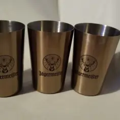 Trzy metalowe kieliszki z logo Jägermeister, przedstawiającym jelenia z krzyżem. Idealne na wodkę z jeleniem.