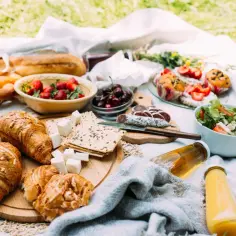 Idealne jedzenie na piknik: świeże croissanty, jagody, sałatka, kiełbasa i napoje.