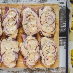 Plastry schabu w sosie z cebulą na desce, obok pieczone ziemniaki.