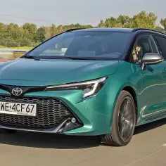Zielona Toyota Corolla kombi jedzie po drodze, za nią widać las.