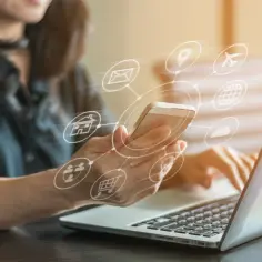 Kobieta z telefonem w dłoni pracuje na laptopie, otoczona ikonami symbolizującymi różne usługi online. Szybkość połączenia, nawet kilkaset **mbps**, umożliwia płynne korzystanie z nich.