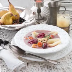 Elegancka czarna polewka z owocami, jak z "Pana Tadeusza", podana na białej zastawie, z gruszkami i śliwkami w tle.