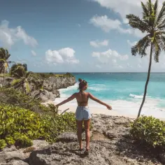 Kobieta z rozłożonymi rękami podziwia turkusowe morze i palmę. Idealne Barbados wakacje.