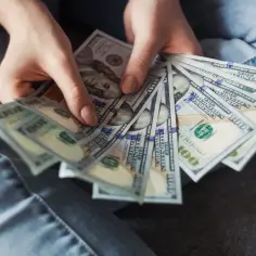 Dłonie trzymające wachlarz banknotów 100-dolarowych. Jak sprawdzić dewelopera? Finanse i inwestycje.