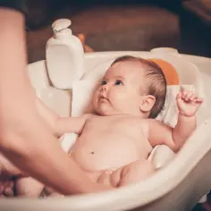 Delikatne mycie noworodka w wanience. Rodzic ostrożnie trzyma dziecko, ucząc się, jak kąpać noworodka.
