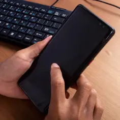 Dłonie trzymają smartfon, obok klawiatura. To przygotowanie do pracy z Samsung DeX, zamieniając telefon w komputer.