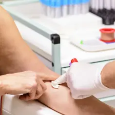 Pobieranie krwi do badań. Ręka pacjentki z wenflonem, pielęgniarka w rękawiczkach przygotowuje probówkę mpv.