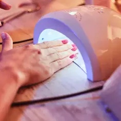 Dłoń z różowymi paznokciami w kropki, utwardzanymi w lampie UV. Efekt bubble nails gotowy!