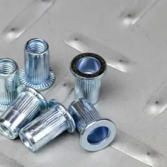 Kilka metalowych nitonakrętek leży na chropowatej, metalowej powierzchni.