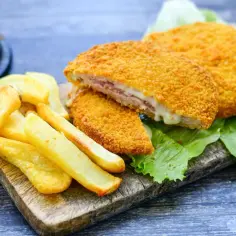 Kotlet po szwajcarsku z serem i szynką, panierowany, podany z frytkami i sałatą.