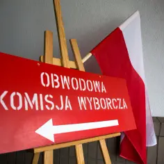 Czerwony znak z białym napisem "OBWODOWA KOMISJA WYBORCZA" i strzałką w lewo, obok polskiej flagi. To ważny element kampanii wyborczej.