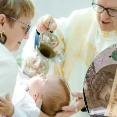 Chrzciny dziecka, ksiądz polewa głowę wodą. Obok banknoty, zastanawiasz się, ile dać na chrzciny od pary?