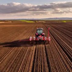 Czerwony traktor z siewnikiem na polu. Zastanawiasz się, ile kosztuje metr ziemi rolnej?