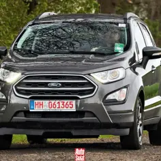Szary Ford Ecosport na leśnej drodze. Kierowca w okularach za kierownicą.