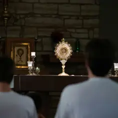 Dwaj młodzi mężczyźni w skupieniu przeżywają adorację Najświętszego Sakramentu.