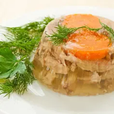 Tradycyjna galareta wieprzowa z marchewką i koperkiem, podana na białym talerzu. Pyszne danie, które przywołuje wspomnienia.