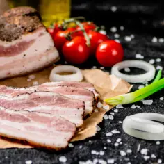 Idealny boczek do carbonary: plastry wędzonego boczku, pomidorki koktajlowe, cebula i szczypiorek na czarnym tle.
