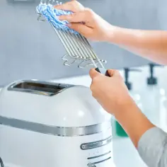 Jak wyczyścić przypalony toster sandwich bez zalewania elektroniki wodą. Ręce czyszczą metalowy ruszt wilgotną ściereczką.