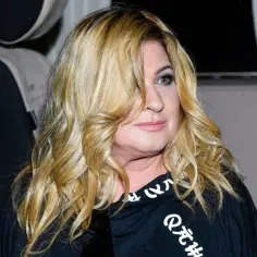 Beata Kozidrak bez peruki, z burzą blond włosów opadających na twarz, w czarnej bluzie z białym napisem.