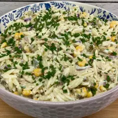 Pyszna sałatka z tuńczykiem i makaronem orzo, z kukurydzą i szczypiorkiem, w ozdobnej misce.