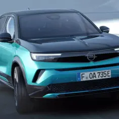 Turkusowy Opel Mokka Electric z czarnym dachem pędzi po drodze.