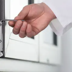 Dłoń z kluczem imbusowym dokonuje regulacji drzwi balkonowych uchylnych, dopasowując zawias.
