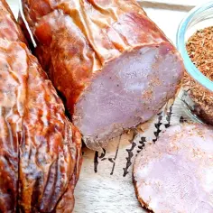 Kiełbasa krakowska przepis: wędzona, pokrojona w plastry, obok miseczka z przyprawami.