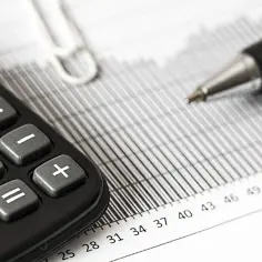 Kalkulator i długopis na dokumentach. Czy podatek od nieruchomości płaci się przelewem podatkowym? Analiza finansowa.