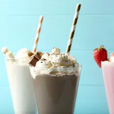 Jak zrobić shake? Trzy pyszne desery: waniliowy z rurkami waflowymi, czekoladowy z kawałkami czekolady i truskawkowy z owocem.