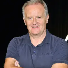 Aleksander Mikołajczak, uśmiechnięty mężczyzna w granatowej koszulce polo, z rękami skrzyżowanymi na piersi.