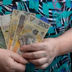 Dłoń trzyma kilka polskich banknotów o nominałach 100 i 200 złotych.