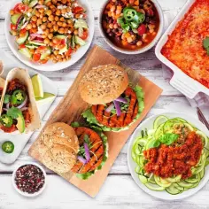 Stół z różnorodnymi wegetariańskimi potrawami: tacos, burgery, sałatki, zapiekanka i zupa.
