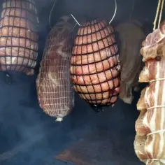 Mięsa w siatkach wiszą w dymie. Czy brzoza nadaje się do wędzenia? Wędzonki nabierają koloru i aromatu.