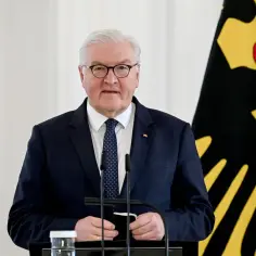 Prezydent Niemiec Frank-Walter Steinmeier w garniturze i krawacie stoi obok flagi Niemiec.