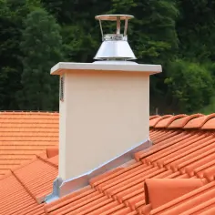 Nowy komin na dachu z pomarańczowej dachówki, na tle zielonego lasu.