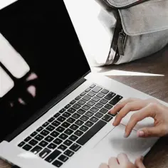 Kobieta siedzi przy laptopie, szukając informacji, jak sprawdzić status bezrobotnego. Obok stoi kubek kawy i pomarańczowy dysk zewnętrzny.