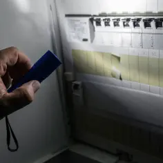 Ręka trzymająca niebieską latarkę oświetla rozdzielnicę elektryczną, pomagając sprawdzić, gdzie jest awaria prądu.