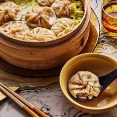 Pyszne pierożki dim sum, czyli to, co jedzą w Chinach, parują w bambusowym parowniku. Na łyżce jeden pierożek z soczystym nadzieniem.
