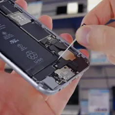 Dłoń wyciąga taśmę z wnętrza otwartego iPhone'a 8, odsłaniając baterię.