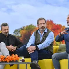 Trzech mężczyzn siedzi na kanapie. Jeden z nich, w niebieskiej koszuli, gestykuluje, opowiadając coś. Obok niego siedzi mężczyzna w kamizelce i okularach. Po drugiej stronie, w czarnej kurtce, siedzi trzeci mężczyzna. To ciekawy hrabi skład.