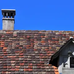 Dwa kominy na dachu z dachówki, wymagające naprawy komina z cegły.
