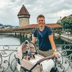 Szczęśliwy tata z wózkiem, na tle zabytkowego mostu i wieży. Pierwsze wakacje z niemowlakiem pełne wrażeń.