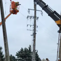Elektryk wysokich napięć w koszu podnośnika pracuje przy linii energetycznej. Obok inny podnośnik z wysięgnikiem.
