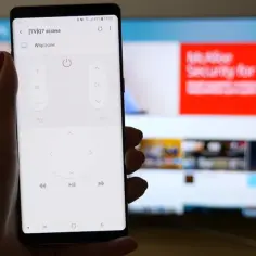 Smartfon z aplikacją do sterowania telewizorem, umożliwiający screen mirroring. Na ekranie telefonu widać przyciski pilota, a w tle telewizor z wyświetloną stroną internetową.