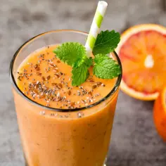 Pomarańczowy smoothie z nasionami chia i siemieniem lnianym, ozdobione miętą. Idealny przepis na to, jak zrobić smoothie.