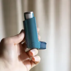 Dłoń trzyma niebieski inhalator z salbutamolem, gotowy do ulgi w ataku astmy.
