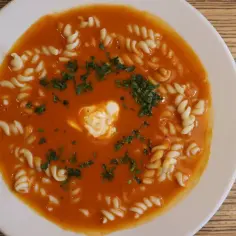 Pomidorowa z makaronem fusilli, udekorowana śmietaną i natką pietruszki, na białym talerzu.