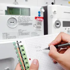 Ręka pisze na notatniku odczyty z liczników energii. Inkasent notuje dane.