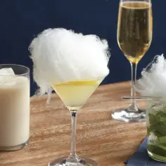Trzy drinki z watą cukrową: biały koktajl, martini z cytryną i mojito. Obok kieliszek szampana.